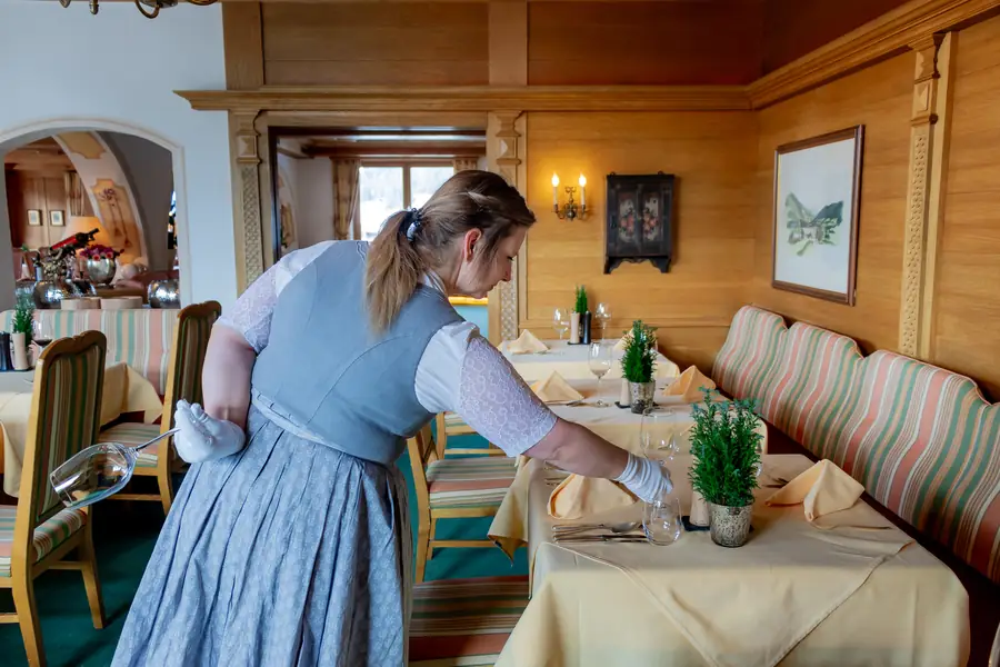 Servicekraft im Dirndl deckt in der Stube die Tische ein