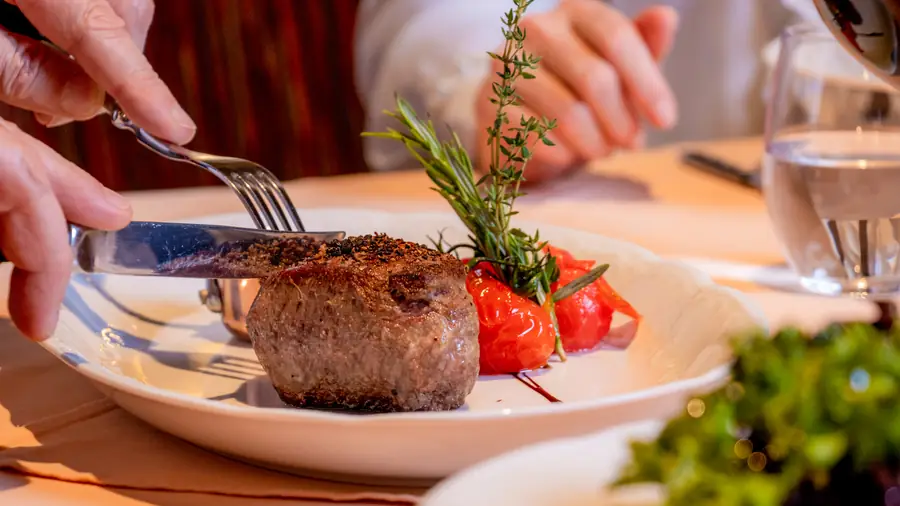 Rinderfilet mit Rosmarinzweig und Kirschtomaten, ein Gast schneidet an