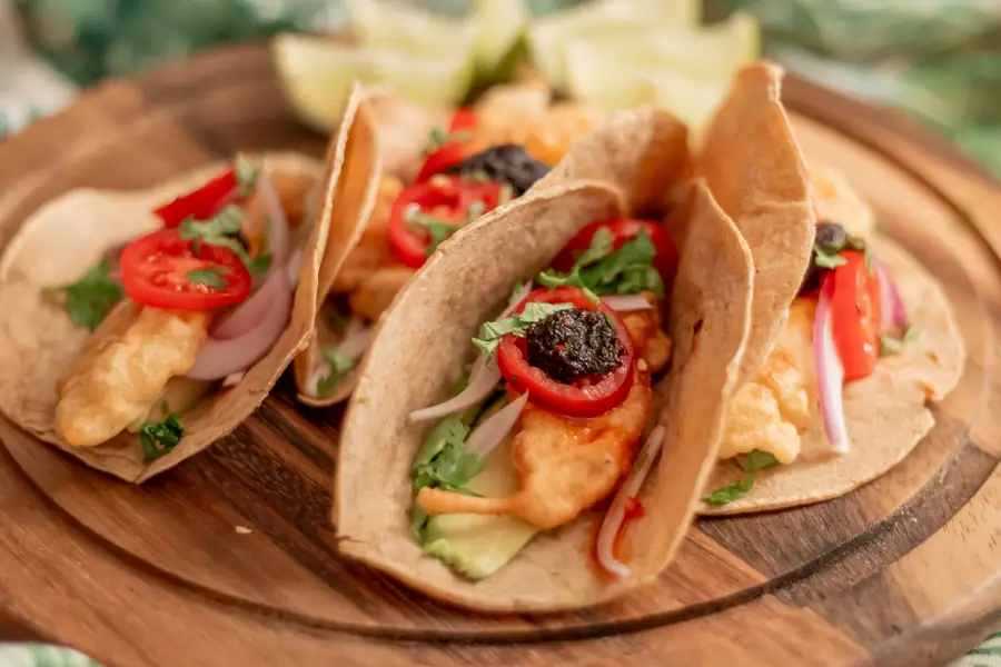 Drei Tacos mit gebackenem Fisch, Tomaten und roten Zwiebeln auf einem Holzbrett